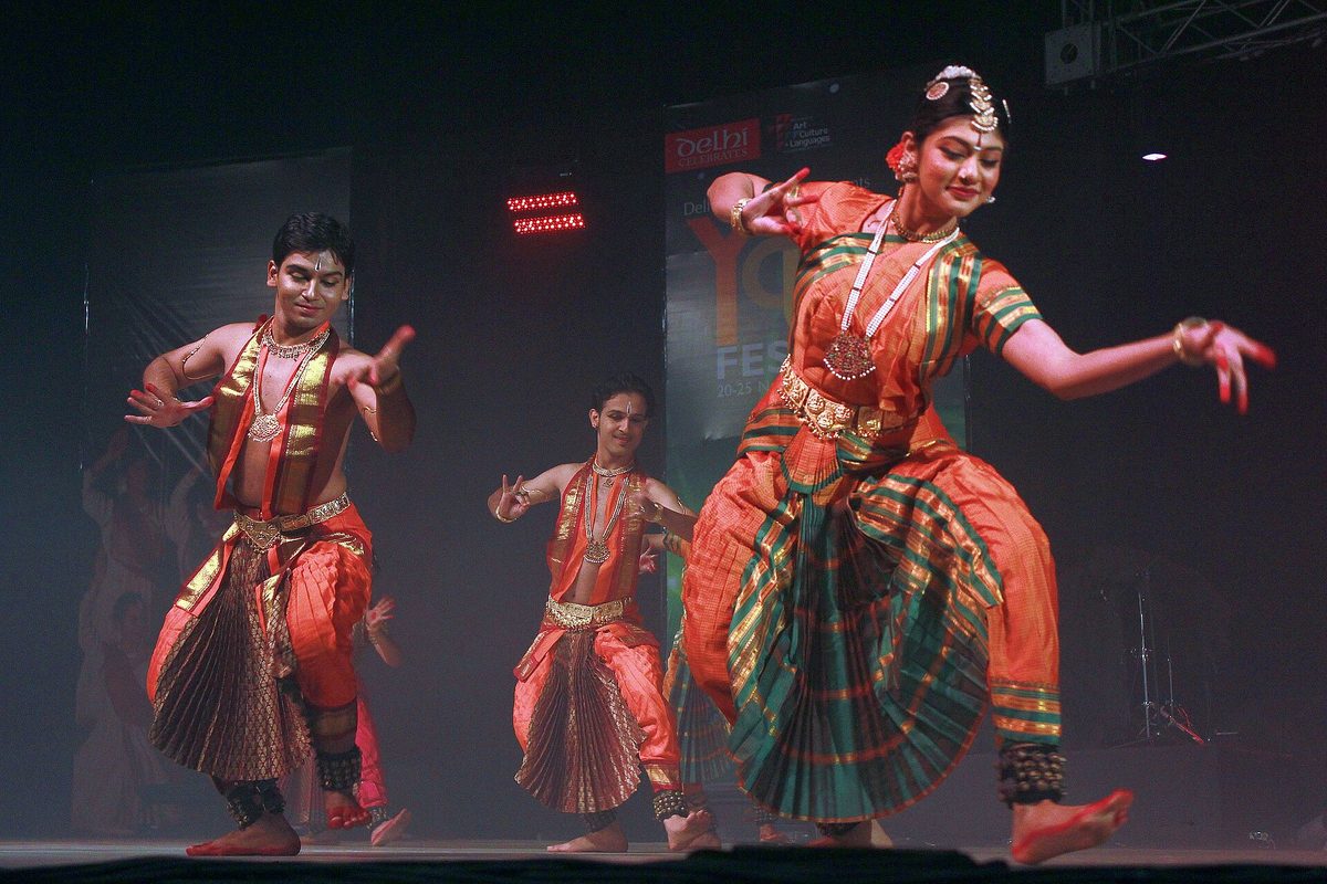 लाल-सुनहरी वेशभूषा में सामूहिक मंच-प्रस्तुति करते भरतनाट्यम नर्तक