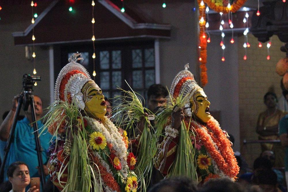 Two daiva performers in golden grass costume and painted faces at a night-time kola ritual