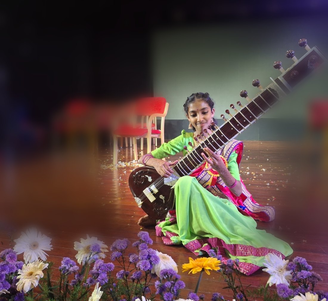 मंच पर बैठकर सितार बजाती देवांगी जन्मोह, अग्रभूमि में फूल