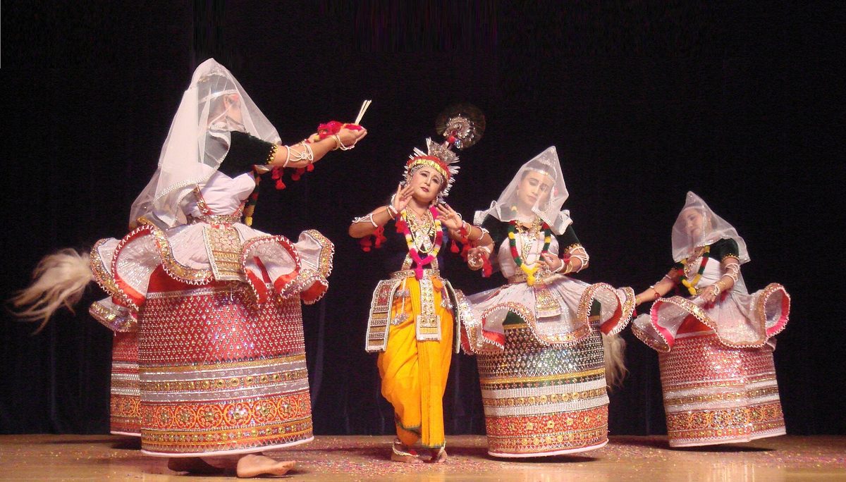 बेलनाकार घाघरे में मणिपुरी रासलीला की नर्तकियाँ, बीच में कृष्ण