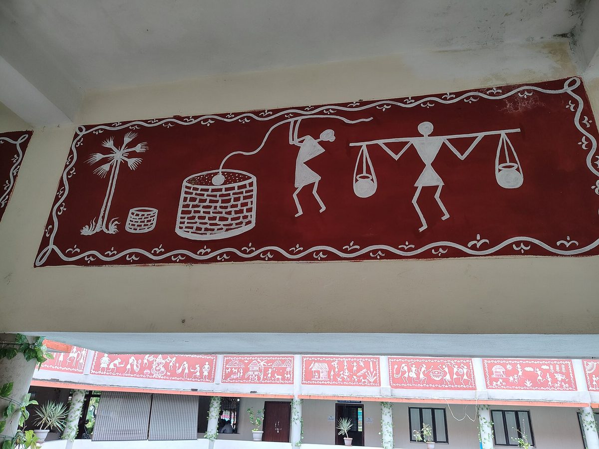 White Warli figures painted on a red wall band of a community building